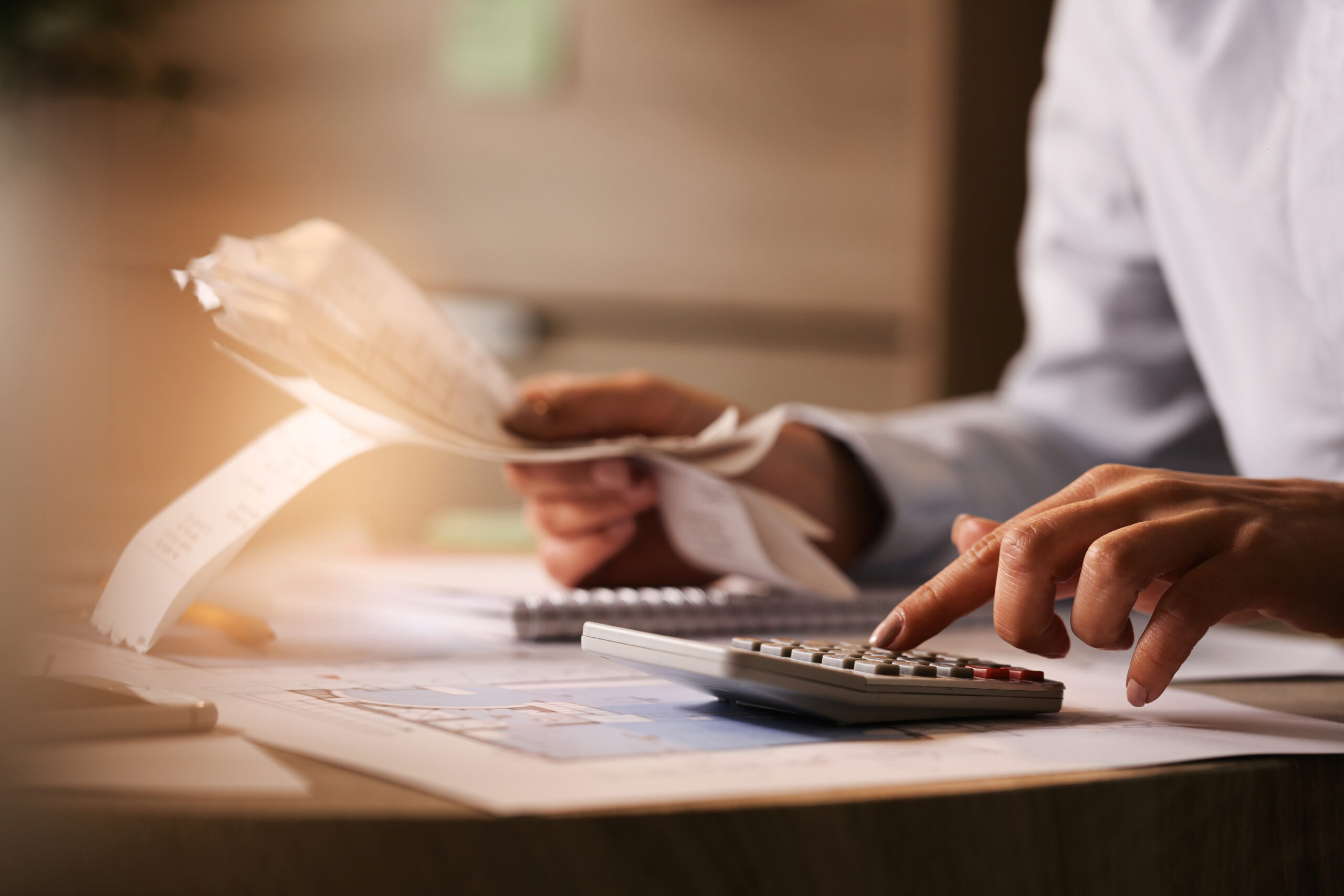 Person calculating expenses with a calculator and reviewing financial documents, symbolizing the process of exploring financing options for air conditioning system replacement.