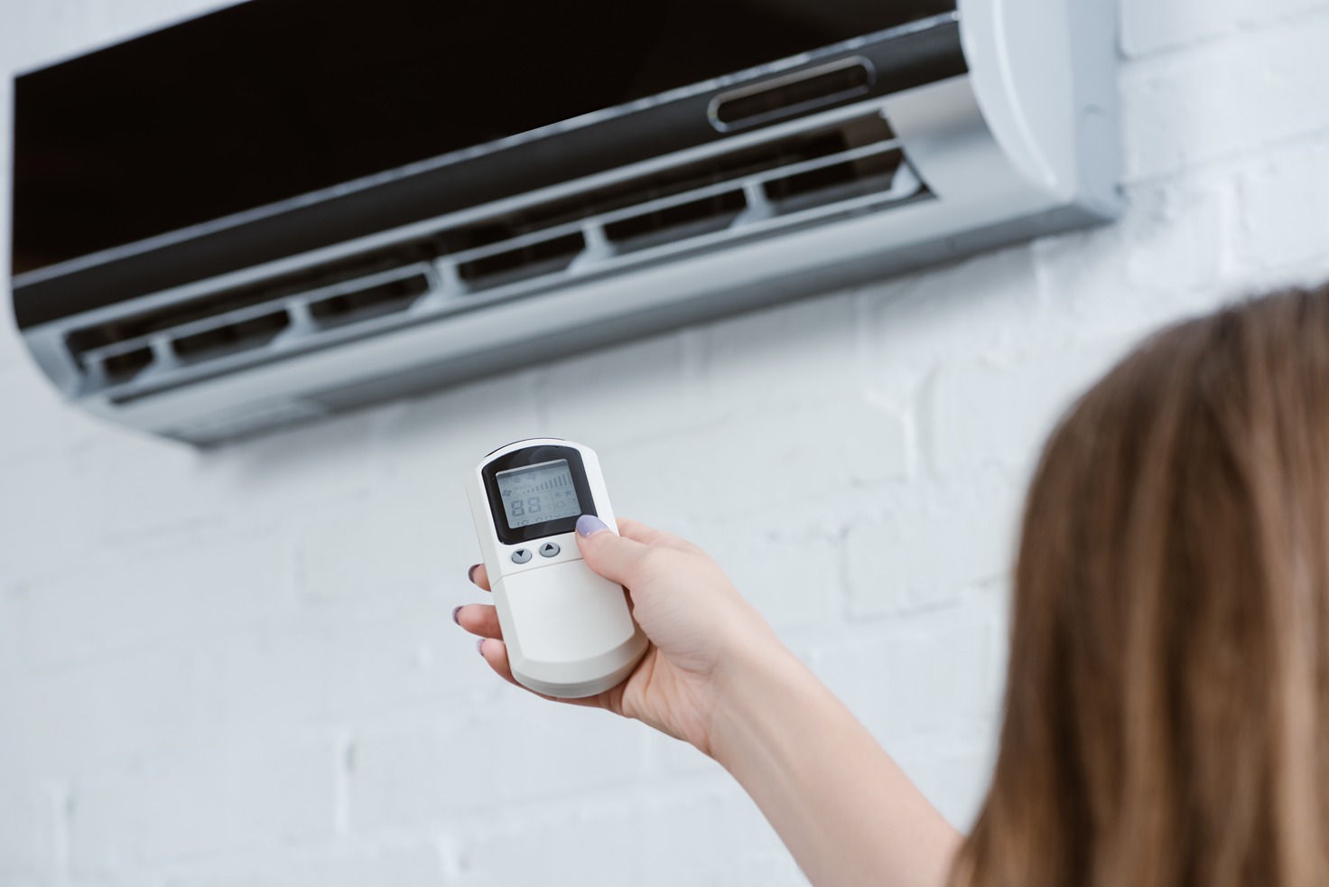 Person using a remote control to adjust a wall-mounted air conditioning unit, emphasizing HVAC maintenance and comfort in home environments.